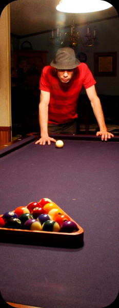 man standing at end of billiards table with bright overhead lighting
